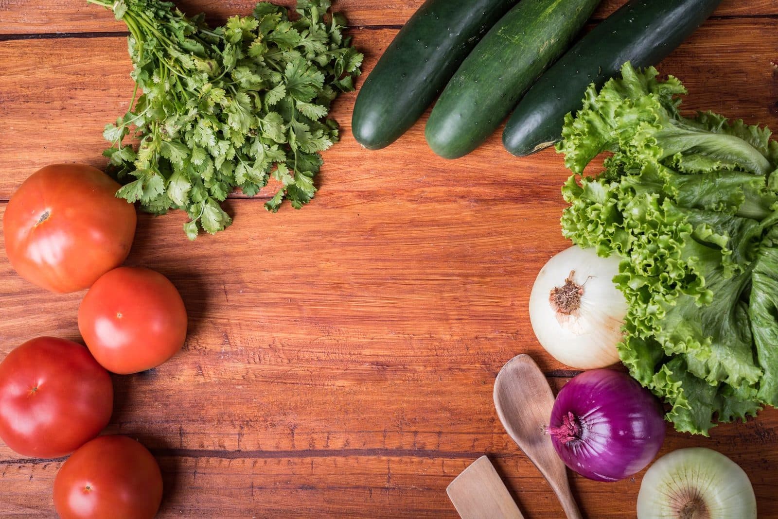 Fresh tomatoes, cucumbers, lettuce, onions and herbs on a wooden cutting board